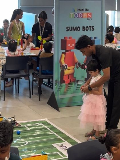 Even our youngest participants get involved. A mentor helps a little girl operate a Sumo Bot at the MetLife event, introducing her to the world of robotics in a playful and accessible manner.
