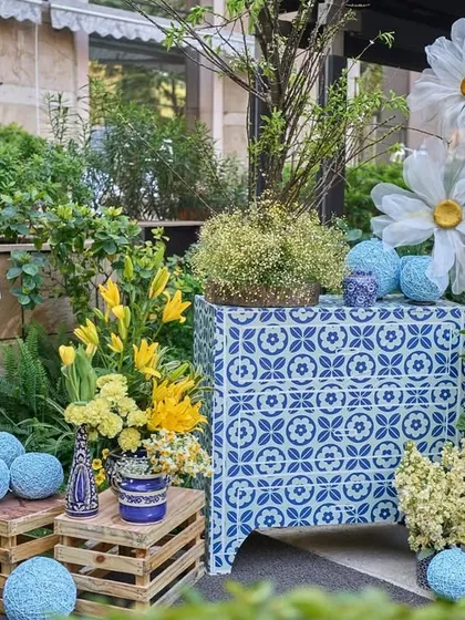 A whimsical decor corner with oversized paper daisies, sunflowers, and blue yarn balls arranged on and around rustic wooden crates.