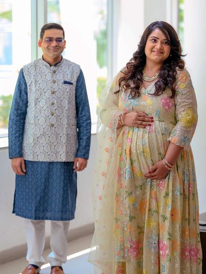 A full-length portrait of the couple, showcasing their coordinated outfits and happy smiles. This shot captures the celebratory feel of their maternity journey.