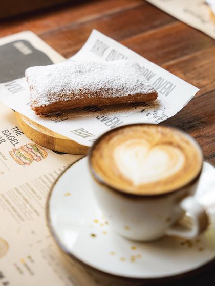 A perfect pairing: a hot cup of coffee with latte art and a freshly fried, powdered sugar-dusted beignet.