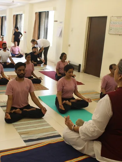 An instructor leads a meditation session, guiding students toward a state of focused calm. We teach yoga as a holistic discipline where mental stillness is as important as physical posture.