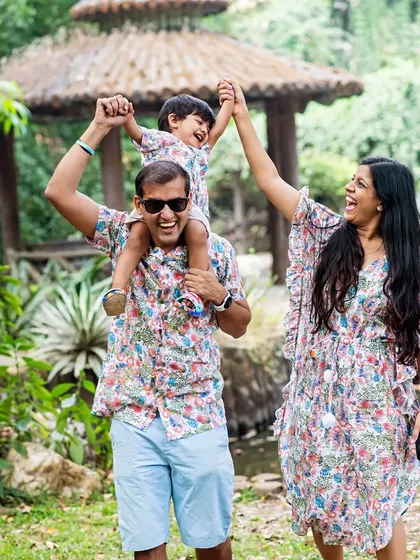 A playful family photo capturing pure joy as the parents lift their son up while walking through a park.