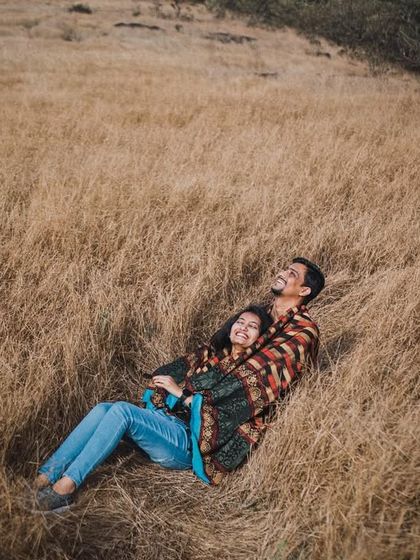 A cozy, intimate moment of the couple lying together in a field of tall, dry grass. This high-angle shot feels natural and captures a quiet moment of shared happiness.