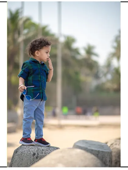 A full-body shot of a toddler standing on the rocks at a Mumbai beach, looking out thoughtfully.