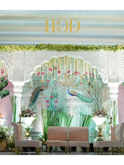 The centerpiece of a Pichwai-themed stage, featuring a hand-painted backdrop of peacocks, elegant seating, and cascading floral strings.