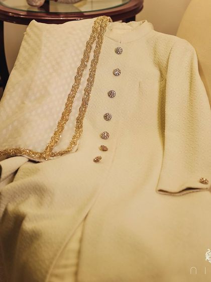 The complete wedding sherwani we designed, laid out to show the custom stole and intricate jeweled buttons. Every element is chosen to create a cohesive and unforgettable groom's outfit.