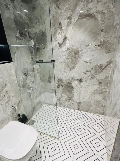 A detail of the bathroom flooring and shower area. The geometric pattern of the floor tiles provides a graphic contrast to the organic veining of the grey marble walls.
