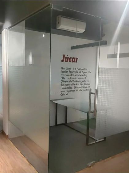 A look inside one of the private glass cabins at the Amigo office. The design is minimalist and functional, with a simple desk and frosted glass for partial privacy. Wall graphics add a unique branding element to each office.