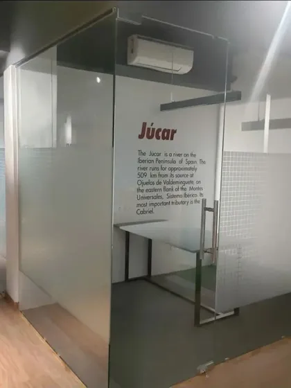 A look inside one of the private glass cabins at the Amigo office. The design is minimalist and functional, with a simple desk and frosted glass for partial privacy. Wall graphics add a unique branding element to each office.