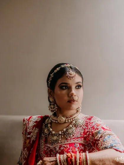 A classic, elegant portrait of the bride, Sakshi, looking away thoughtfully, her intricate jewelry and red lehenga beautifully captured.