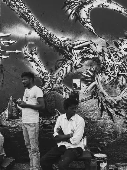 A black and white photograph capturing a moment of pause in front of an intricate, almost monstrous, graffiti piece. The high contrast of the photo emphasizes the detailed linework of the art.