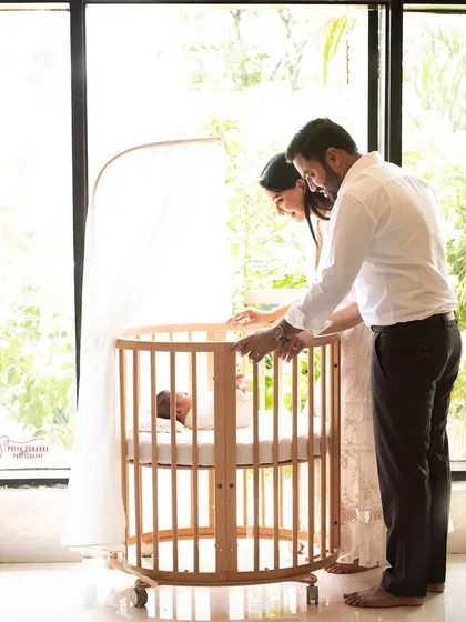 A lifestyle newborn session in the comfort of your own home. Here, new parents admire their baby sleeping peacefully in a beautiful wooden crib by the window.