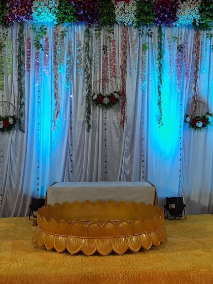 A close-up of the Haldi ceremony stage, featuring a traditional 'urli' for the rituals, set against a lit backdrop with hanging floral decor.