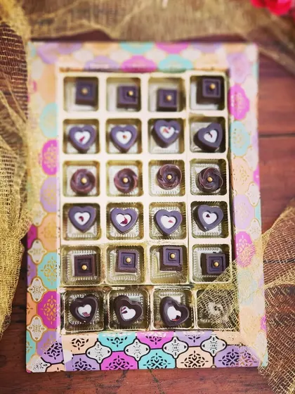 A box of our handcrafted artisan chocolates in a vibrant, traditional Indian print box. The heart and square shaped chocolates are meticulously decorated, making them a beautiful gift.