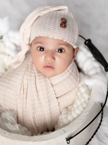 An alert newborn with captivating eyes, swaddled in a neutral wrap. This portrait in a white bucket shows that we capture both sleepy and awake moments beautifully.
