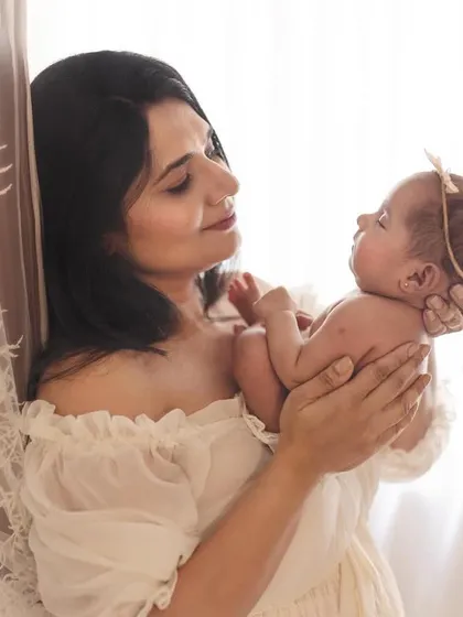 A mother holds her newborn, gazing at her with pure adoration. The soft, natural light from the window wraps around them, creating a dreamy, ethereal feel.