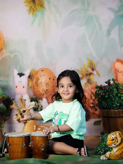 This two-year-old is making some noise in our jungle theme, playing on a set of bongo drums surrounded by her favorite animal friends.