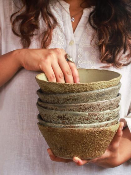 A stack of bowls from 'The Rock Collection,' held in hand to show their unpolished, earthy texture and gentle details.