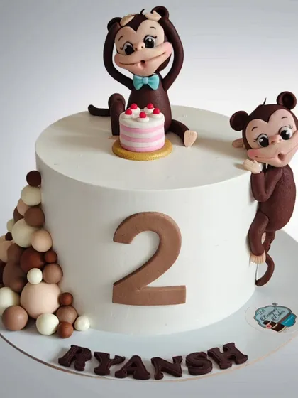 A minimalist and cute monkey-themed cake for a second birthday. The clean white cake is accented with two adorable fondant monkeys and chocolate spheres.