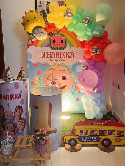 A colorful Cocomelon theme for a first birthday, complete with a character-filled backdrop, a rainbow balloon arch, and themed pedestals.