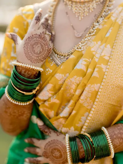 A close-up on the details: the intricate henna, the green bangles, and the rich texture of the yellow silk saree.