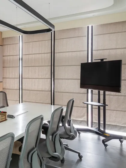 The conference room is equipped with a mobile screen for flexible presentation setups. The fabric roman blinds allow for controlled natural light, ensuring the room is comfortable for meetings at any time of day.