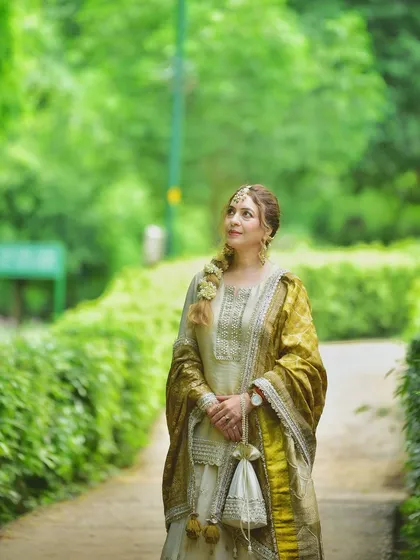 A classic portrait in a lush green pathway. The contrast between the off-white lehenga and the vibrant greenery makes the subject stand out beautifully.