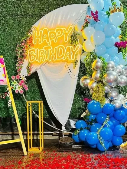 An outdoor birthday celebration with a welcome sign and a backdrop of blue and silver balloons mixed with flowers.