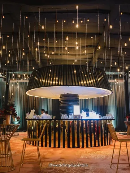 A statement bar can be the centerpiece of a great party. For this modern reception, we designed a dramatic circular bar with a black and gold aesthetic, crowned by a custom light fixture and surrounded by a ceiling of hanging bulbs to create a chic nightclub vibe.