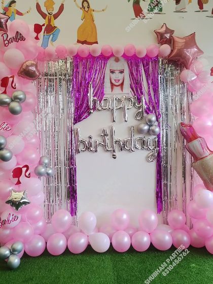 A glamorous Barbie themed birthday party with a pink and silver balloon arch and a shiny curtain backdrop.