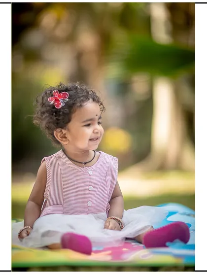 A lovely candid portrait of a little girl with curly hair, smiling during her outdoor photoshoot on a colorful play mat.