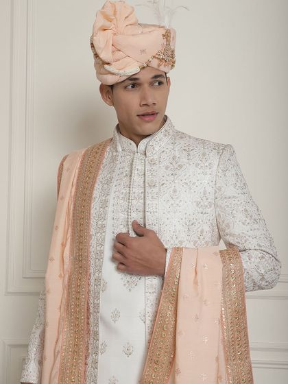 An ivory sherwani paired with a soft peach stole and turban. This combination is perfect for a summer wedding, offering a light, airy, and elegant aesthetic for the modern groom.