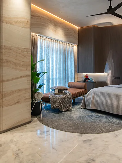 This bedroom at World View Apartments embodies quiet sophistication, where creamy neutral colors and woody browns set a calming foundation. A woven-textured vanity chair and seamless marble-clad column add tactile richness that feels both warm and luxurious.