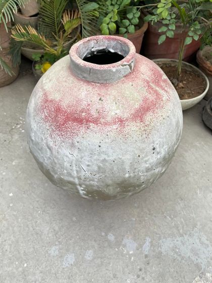 A large, rustic pot with a weathered red and white surface. This piece has the feel of an ancient artifact, perfect as a statement planter in a garden.