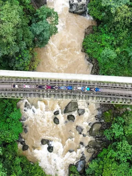 An iconic top-down shot of the Yedakumari railway bridge in Sakleshpur, with a group of trekkers crossing over the rushing river below.