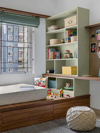 A view of the kid's room in 'Poorna', showing the platform bed with storage drawers, a toy storage unit, and the adjacent study area.