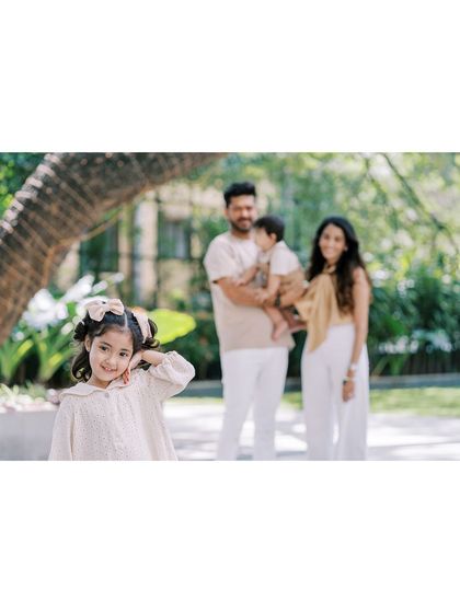 A little girl strikes a pose for the camera, with her family in the background. It's fun to see their personalities emerge during a shoot.