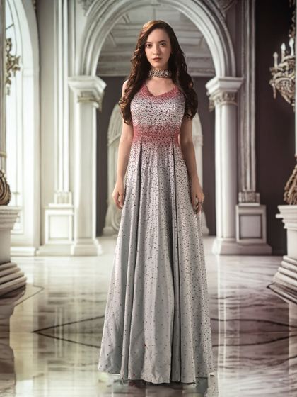 A grand palace hall, projected as a backdrop, lends a sense of scale and majesty. The lighting is kept soft and even to highlight the delicate details of the gown.