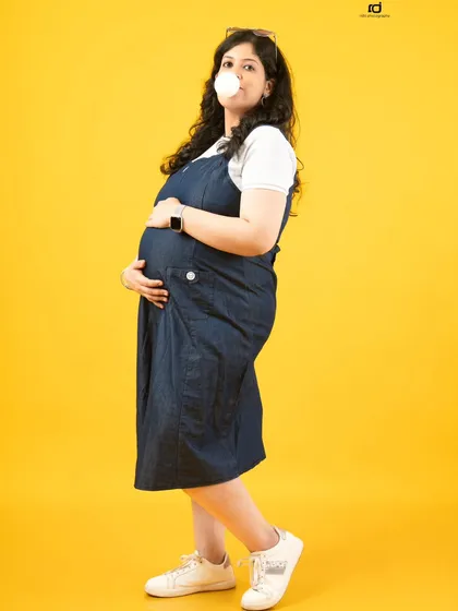 A playful and confident pose. Blowing a bubble adds a touch of fun and personality to this casual maternity shot, showing that pregnancy style can be anything you want it to be.