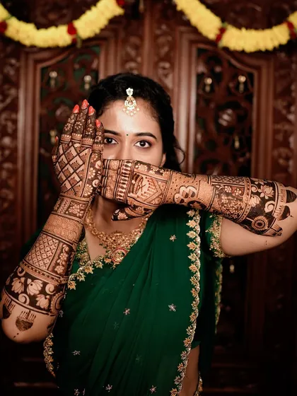A classic peek-a-boo pose from the bride in the green saree, highlighting the intricate details of her henna.