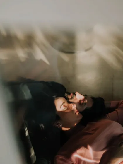A couple rests together, bathed in the warm, patterned light of the sun. This artistic and peaceful candid moment captures a feeling of complete comfort and serenity.