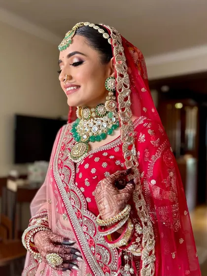 A joyful bride in her red lehenga, her smile lighting up the room. The makeup is designed to be radiant and long-lasting, perfect for a day full of happy moments.