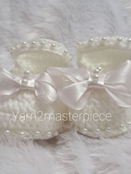 A top-down view of the white satin bow booties, highlighting the beautiful shape and the securely attached pearl and bow embellishments.