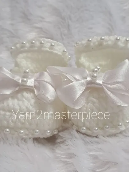 A top-down view of the white satin bow booties, highlighting the beautiful shape and the securely attached pearl and bow embellishments.