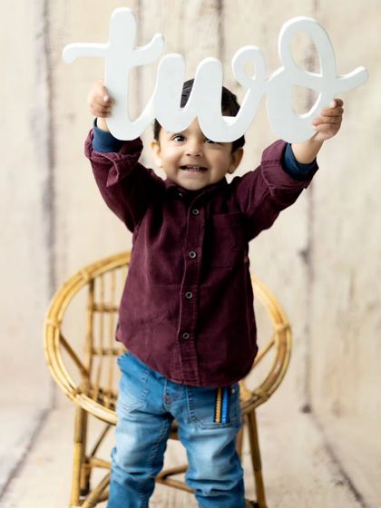 Pure excitement for turning two. This little boy holds up a 'two' sign with a huge smile on his face.