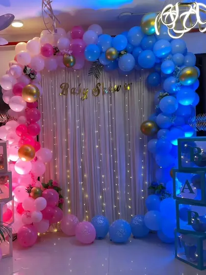 A classic gender reveal baby shower setup. The decoration features a balloon arch split between pink and blue, with matching "BABY" blocks on each side and a "Baby Shower" foil balloon in the center.
