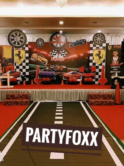 A grand car racing theme setup with a custom printed road leading to the stage. The backdrop features Ferrari branding, checkered flags, and car cutouts.