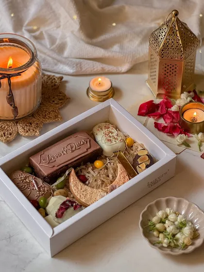 A white gift box filled with an assortment of Eid treats, including decorated cookies, stuffed dates, and chocolate bars. This is a perfect sampler of my Eid collection.