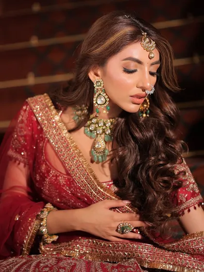A soft, contemplative moment. The side profile highlights the cascading hair and the stunning emerald and polki earrings, adding to the overall regal feel of the bridal look.