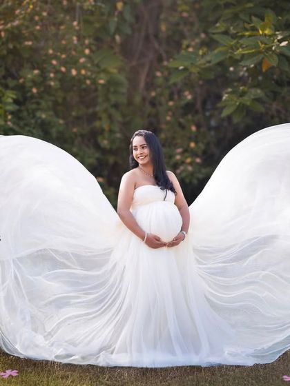 The white gown's fabric is tossed to create angelic wings, a stunning and creative shot in a natural setting.